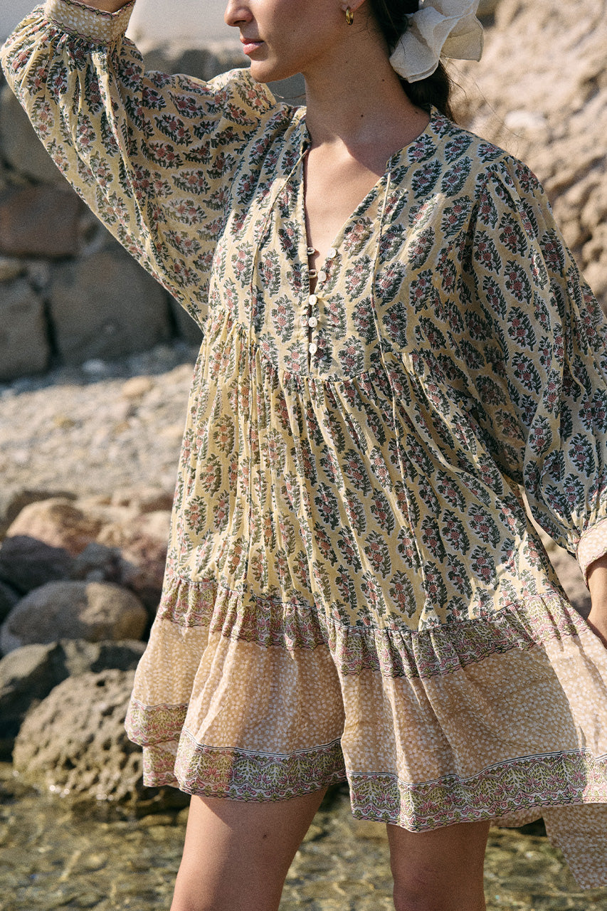 Close-up of woman near rocks and water wearing the Daughters of India Bhoomi Mini Dress in Meadow, shielding her eyes, showcasing the detailed V-neckline and billowed sleeve design