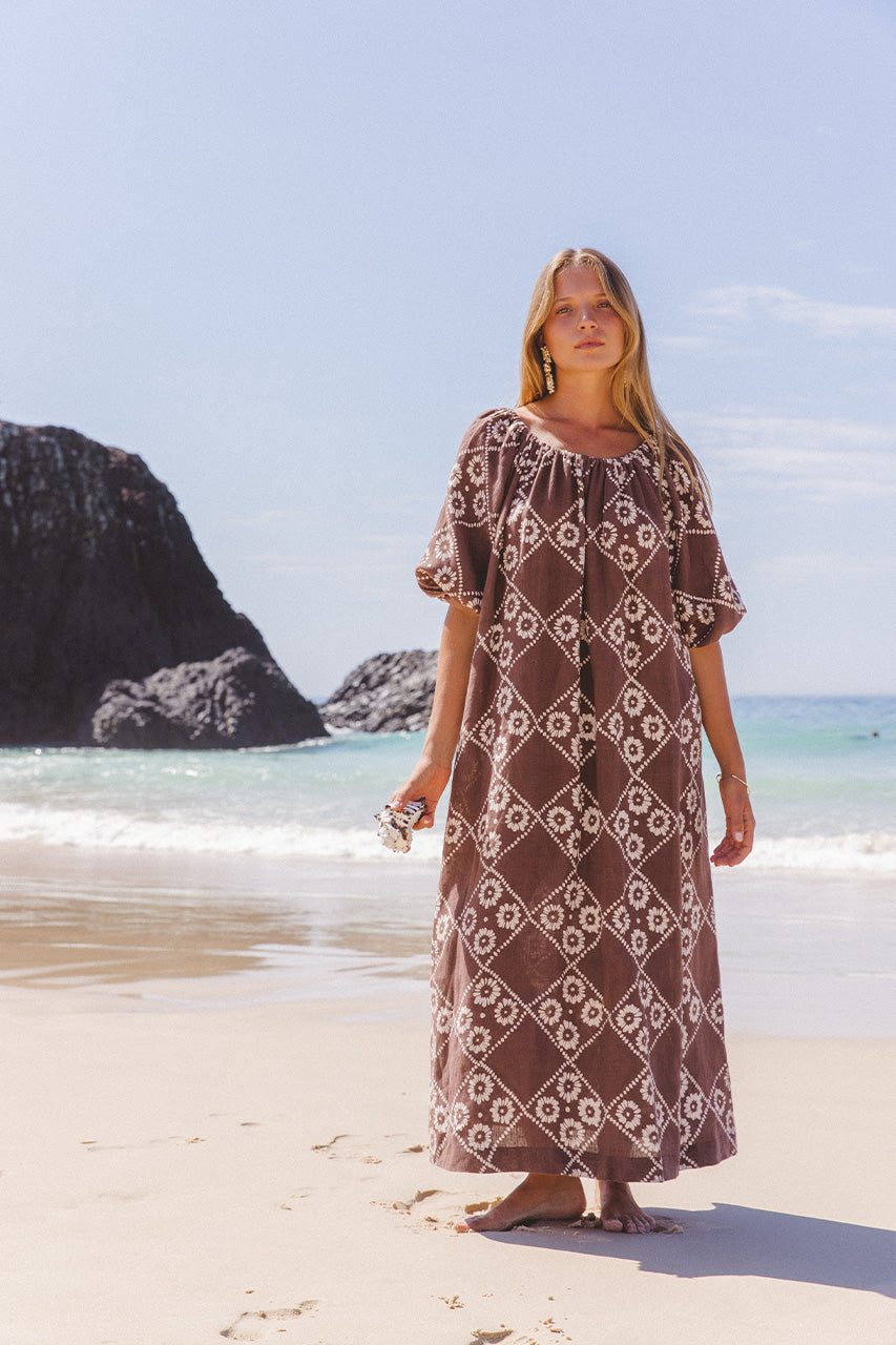 Dahlia Maxi Dress Maple — full length beach styling with rocky headland, on-shoulder neckline option, hand block print linen in maple brown | Daughters of India
