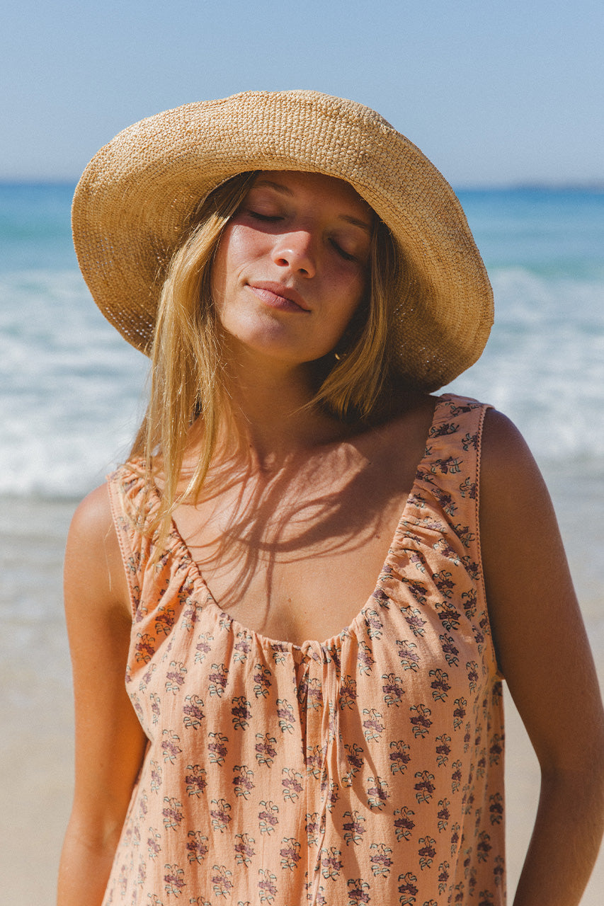 Sundress Midi Peach — model seated outdoor, relaxed pose showing gathered skirt fall, peach floral block print cotton dress, sleeveless sundress, artisan made Jaipur India | Daughters of India