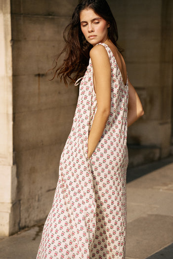 Side profile of woman against stone wall wearing the Daughters of India Sundress Midi in Peony, showing the full midi length and sleeveless silhouette
